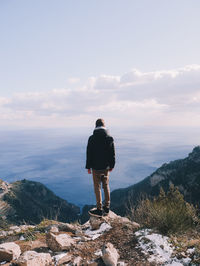 Rear view of man standing on rock against sky