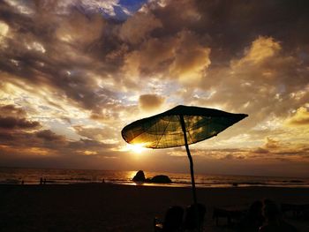 Beach umbrella against cloudy sky at sunset