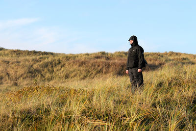 Man wearing jacket standing on grassy field against sky