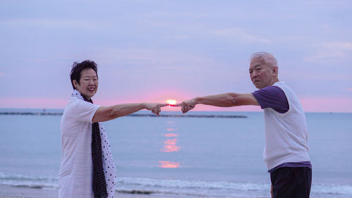Portrait of couple standing at sea against sky during sunset