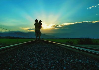 Man standing on railroad track against sky during sunset