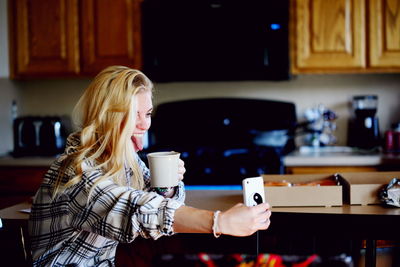 Cheerful woman taking selfie while drinking coffee at home