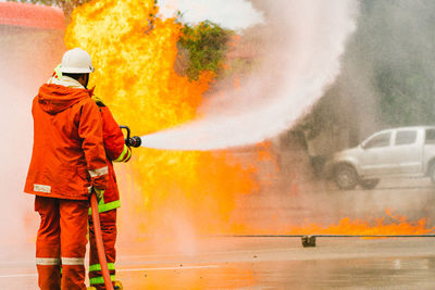 Rear view of firefighter spraying water on fire while standing at street