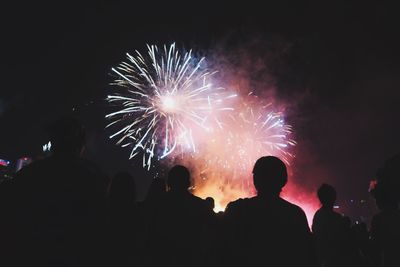 Low angle view of silhouette people looking at firework display at night