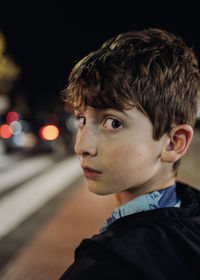 Headshot portrait of a young boy lost at night looking back scared