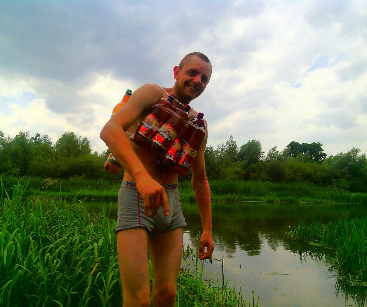 tree, sky, cloud - sky, grass, standing, outdoors, real people, field, one person, water, leisure activity, day, nature, casual clothing, growth, reflection, lifestyles, men, full length, smiling, young adult, people