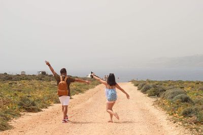 Rear view of friends walking at beach against sky