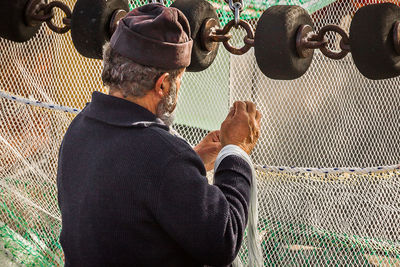 Rear view of man looking at chainlink fence