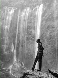 Side view of woman standing on rock against waterfall
