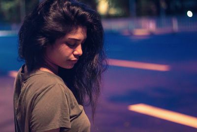 Close-up of young woman looking down against trees at night