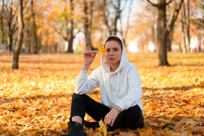 Portrait of woman sitting on leaves covered land during autumn