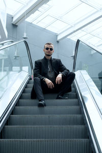 Low angle view of young man sitting on escalator