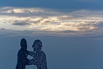 Low angle view of molecule man against cloudy sky