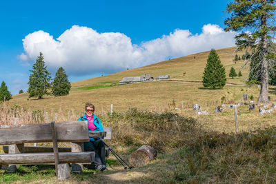 Man sitting on bench on field against sky