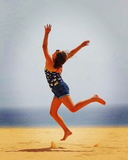 Young woman jumping on beach against sky