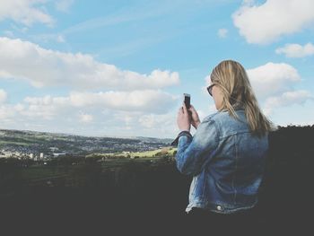 Teenage girl photographing landscape against sky