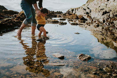 Low section of father and daughter wading in puddle against sky