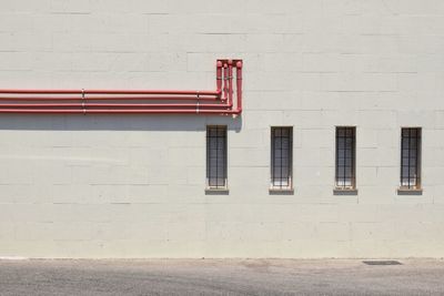 White wall of building with red pipes and four littles windows