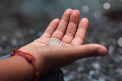 Close-up of child hand holding coin outdoors
