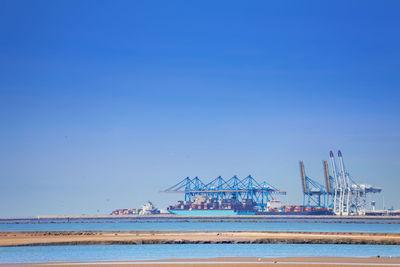 Cranes at commercial dock against clear blue sky