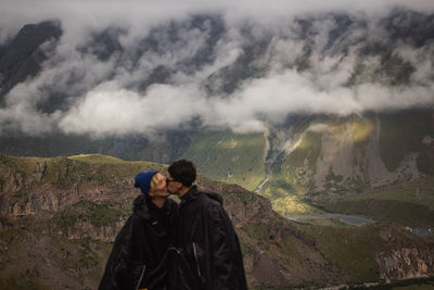 People kissing on mountain against sky during winter