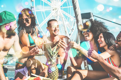 Happy friends toasting drinking glasses in sunny day