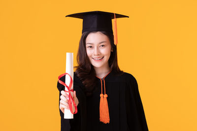Portrait of smiling young woman against yellow background