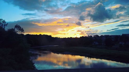 Silhouette trees on field against cloudy sky at sunset