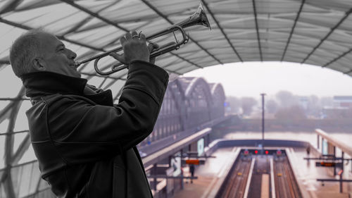 Man playing trumpet while standing at railroad station