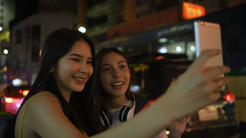 Portrait of smiling young woman using smart phone at night