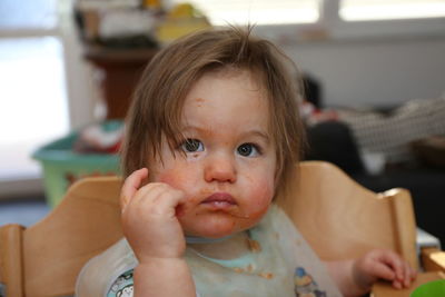 Close-up of cute baby girl with messy face looking away while sitting on chair at home