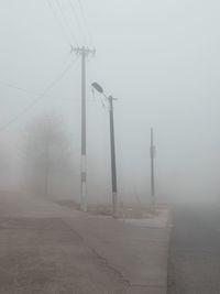 Electricity pylon by road against sky during foggy weather