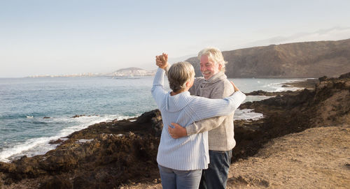 Happy senior couple dancing on rocky coastline