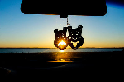Silhouette decoration on rear-view mirror of car against clear sky