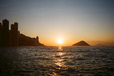 Scenic view of sea by buildings against sky during sunset