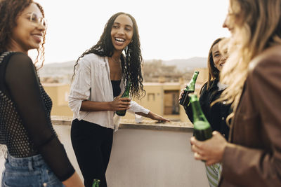 Carefree female friends holding beer bottles in party on building rooftop