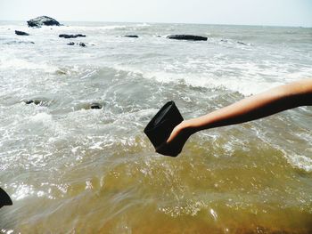 Close-up of hand in sea against sky