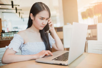 Young woman using phone while sitting on table