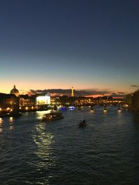 Illuminated buildings by sea against clear sky