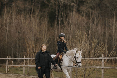 Girl horseback riding with female instructor walking along her