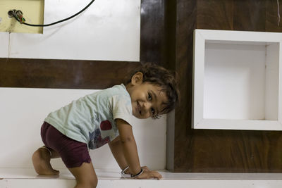 A small child climbing on a small wooden table looking back and showing the joy of climbing