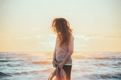 Mature woman standing at beach against sky during sunset