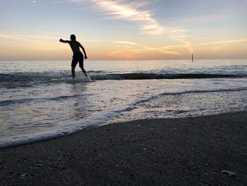 Silhouette man standing on beach against sky during sunset