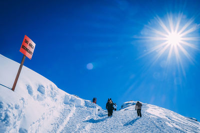 People on snowcapped mountain against blue sky on sunny day