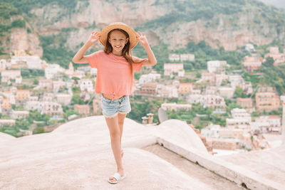 Full length portrait of smiling young woman standing against built structure