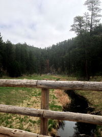 Wooden fence on field by trees against sky