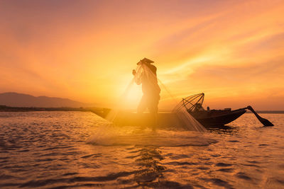 Man fishing in sea against orange sky