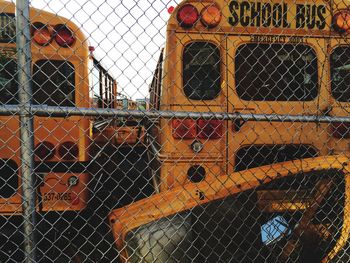 School buses in parking lot seen through chainlink fence