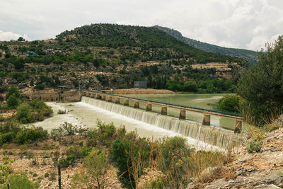 Bridge over river with green hill against sky