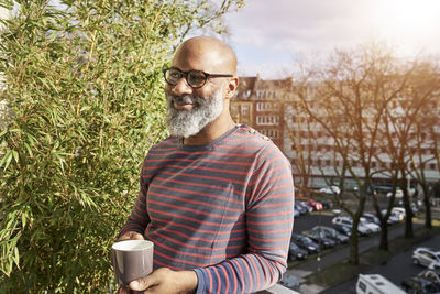 Mature amn standing on balcony, drinking coffee